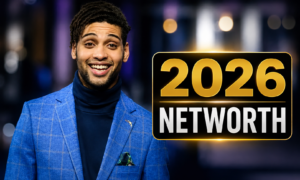 Rohan Nedd smiles in a stylish blue suit at a red carpet event, featured in the article "Rohan Nedd Net Worth 2026: Rising Star's Career & Wealth."